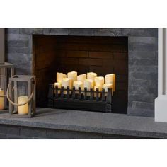 several lit candles sit in front of a fireplace