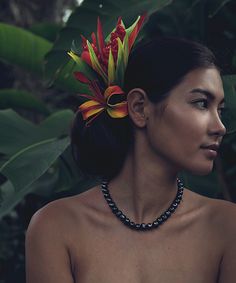 a woman wearing a necklace with flowers on it's head and an orange flower in her hair