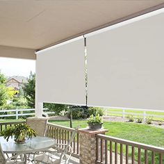 an outdoor patio with white shades on the windows and table, chairs, and potted plants