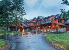 a large wooden house sitting on top of a lush green field next to a forest