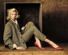 a woman sitting in a wooden box with her legs crossed and red shoes on the ground