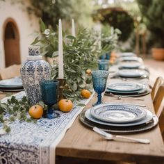 the table is set with blue and white plates, silverware, oranges and candles