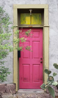 a bright pink door is open in front of a stucco wall and green planters