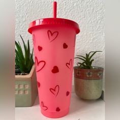 a pink cup with hearts on it next to some succulents and a potted plant