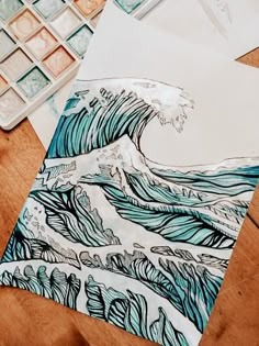 a drawing of a wave on paper next to watercolors