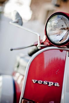 a red vespa scooter parked in front of a building with its lights on