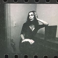 a black and white photo of a woman sitting in front of a mirror with her hands on her head