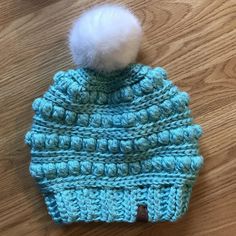 a crocheted hat with a white pom - pom on top sitting on a wooden floor