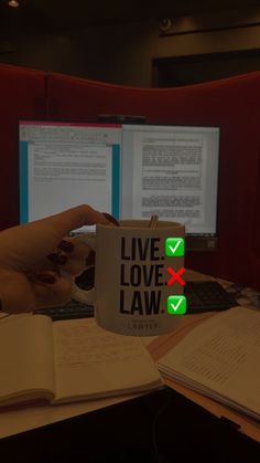 a person holding a coffee mug with the words live love law on it in front of two computer monitors