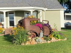 an old truck with flowers in the bed is parked on some grass near a house