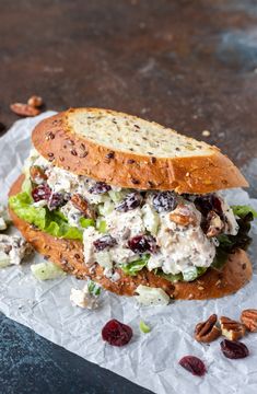 a chicken salad sandwich with cranberries and pecans on a piece of wax paper