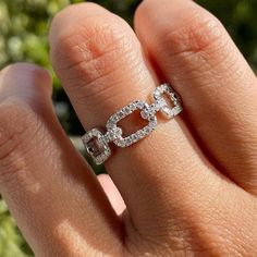 a woman's hand with a diamond ring on top of her finger, in front of some bushes