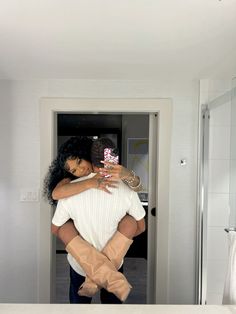 a woman holding a child in her arms while standing in front of a bathroom mirror