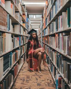 a woman in a graduation cap and gown sitting on the floor next to bookshelves