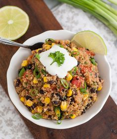 a white bowl filled with rice and vegetables on top of a wooden cutting board next to lime wedges