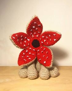 a crocheted red and white flower sitting on top of a wooden table