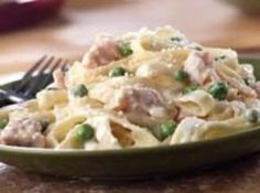 a green plate filled with pasta and peas on top of a table next to a fork