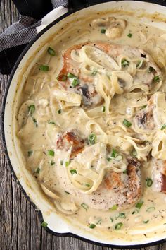 a skillet filled with pasta and meat covered in gravy on top of a wooden table