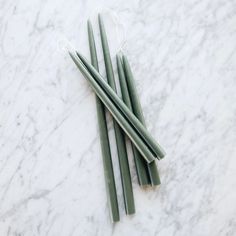 three green candles sitting on top of a white marble counter next to twine string