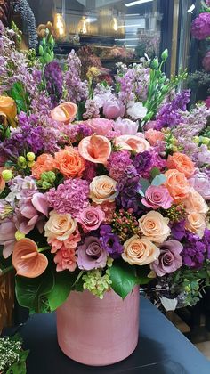 a pink vase filled with lots of purple and orange flowers on top of a table