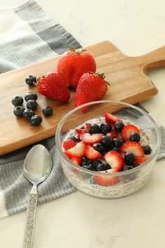 berries and blueberries are in a bowl next to a cutting board with spoons