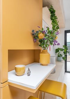 a vase with flowers sitting on top of a table next to two yellow stools