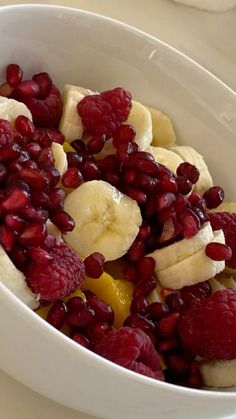 a white bowl filled with bananas, raspberries and oranges on top of a table