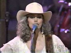 a woman wearing a cowboy hat singing into a microphone