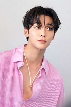 a woman with black hair wearing a pink shirt and gold necklace, looking off to the side