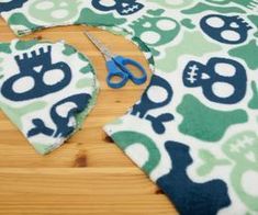 scissors are sitting on top of a green and white skull print tablecloth that has been cut out