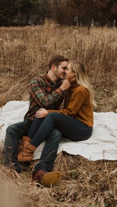 an engaged couple sitting on a blanket in the middle of a field with tall grass