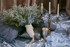 an arrangement of flowers and candles on a silver cloth covered table with sequins