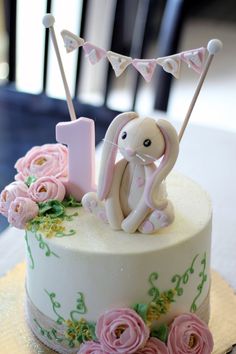 a white cake decorated with pink flowers and a small bunny on top is the number one