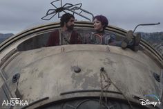 two people sitting in the back of an old airplane looking at each other with mountains in the background