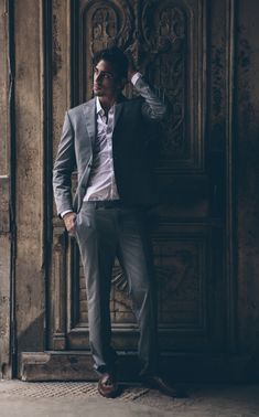 a man standing in front of a wooden door with his hand on his head and looking off to the side