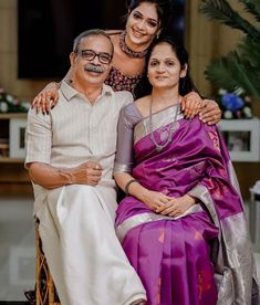 an older man and two younger women sitting on a chair in front of a plant