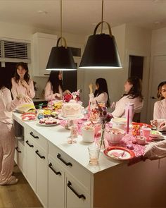 a group of women in pink robes standing around a kitchen counter with food on it