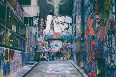 a narrow alley with graffiti all over the walls and below it is a person walking down one side