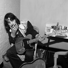 a man sitting in a chair holding a guitar and looking at the camera with his hand on his mouth