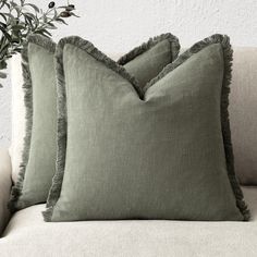 two green pillows sitting on top of a couch next to a vase filled with flowers