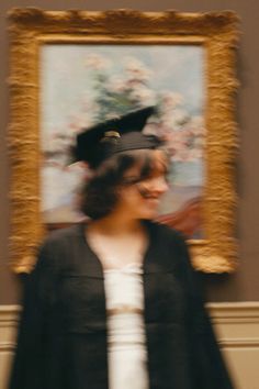 a blurry photo of a woman wearing a graduation cap and gown in front of a painting