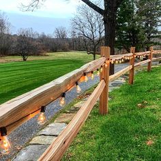 a wooden fence with lights on it in front of a grassy field and tree lined path