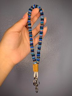 a hand holding a blue beaded lanyard with a wooden clip on the end