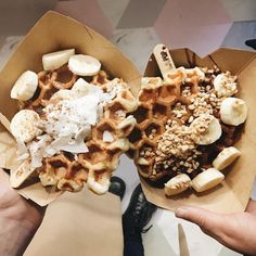 two waffles with bananas, nuts and whipped cream in paper containers on a table