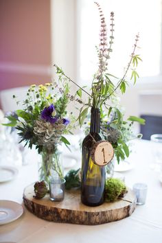 two vases filled with flowers on top of a wooden board at a dinner table