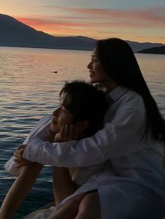 two people sitting on the back of a boat at sunset