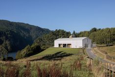 a white house sitting on top of a lush green hillside next to a lake and forest