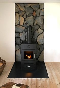 a wood burning stove sitting inside of a living room next to a stone wall and wooden floor