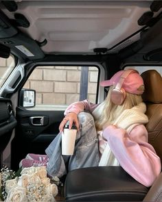 a woman sitting in the back seat of a car with headphones on and holding a coffee cup