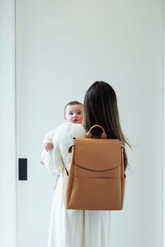 a woman holding a baby in her back pack and looking at the wall behind her